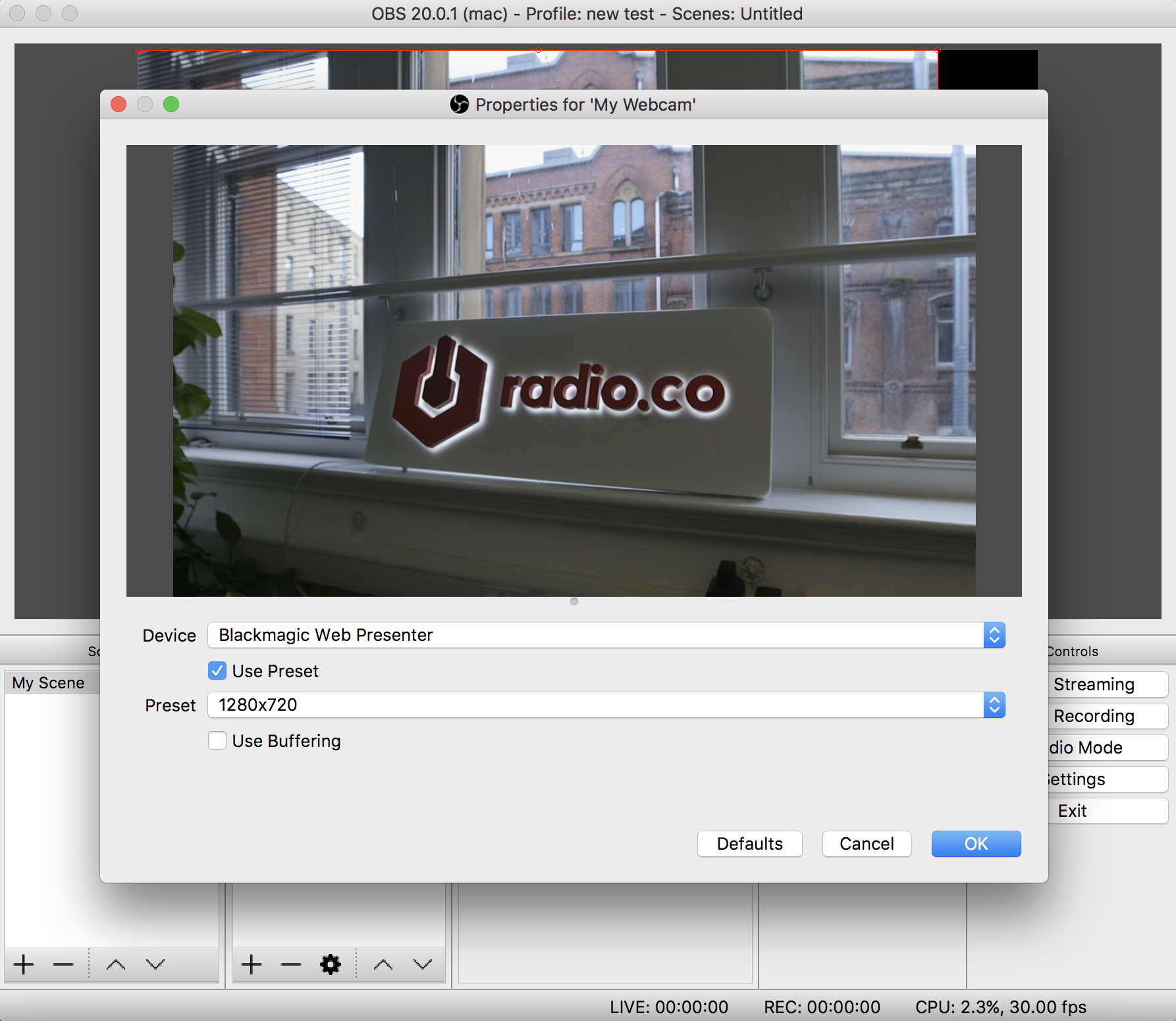 A screenshot illustrating how choosing a video device in OBS will appear. It has an image of what the webcam can see, a Radio.co logo and a studio in this instance, and boxes with preset devices beneath it. There is a highlighted 'OK' that you must click in the lower corner.